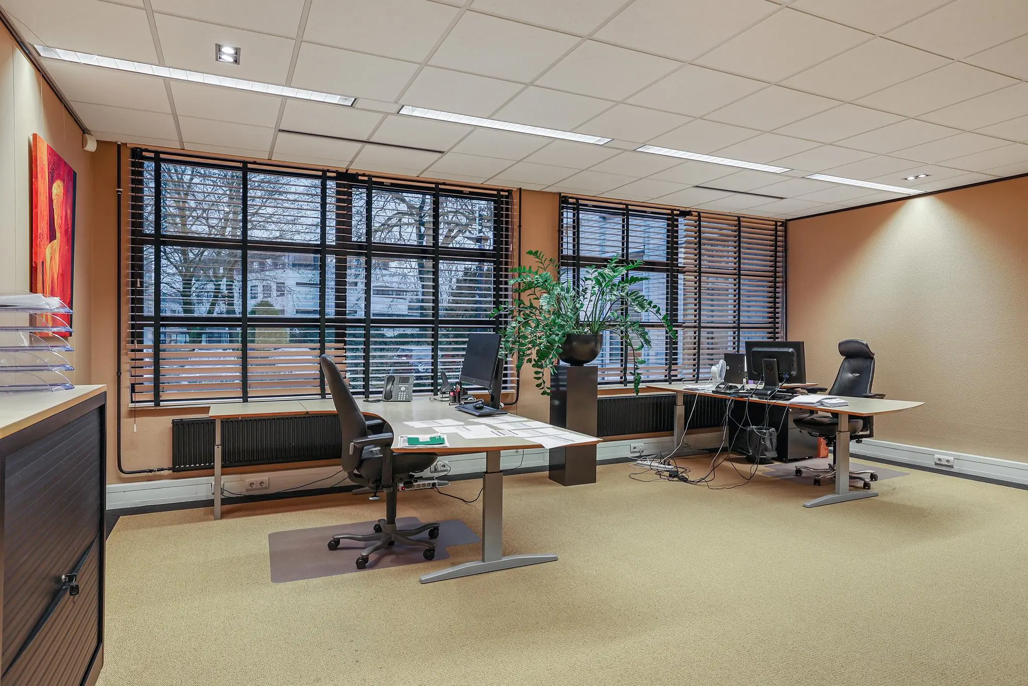 Modern kantoorinterieur aan de Oude Utrechtseweg met bureaus, stoelen, computers en grote ramen met jaloezieën.